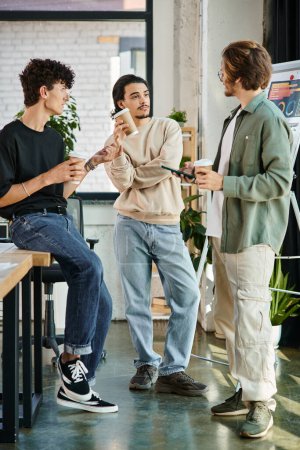 Photo for Young men in their 20s sharing ideas and holding coffee to go in modern office, startup team - Royalty Free Image