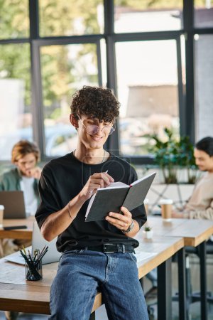 Curly-haired man with glasses smiling and taking notes in a dynamic office space, startup ideas
