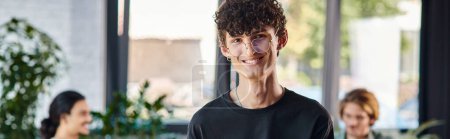 happy and curly-haired man smiling and taking notes in a dynamic office space, startup banner