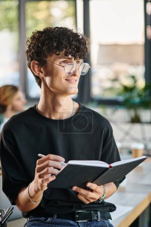 Curly-haired startup team member with glasses smiling and taking notes in a dynamic office space
