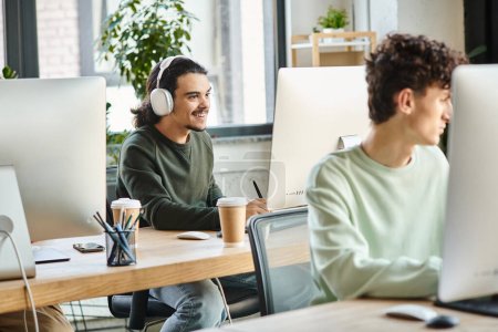 glücklicher junger Profi mit Kopfhörern bei der Retusche am Computer in der Nähe eines Kollegen