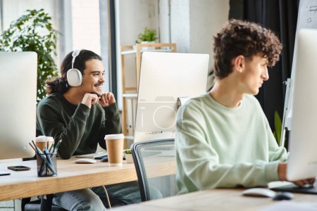 Jeune homme avec écouteurs engagés dans le travail de retouche sur un ordinateur près d'un collègue au bureau