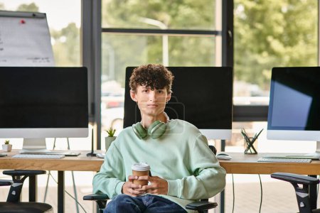 young man with curly hair sitting in office chair and holding coffee, post production team member