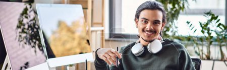 Relaxed young man with stylus pen smiling at a startup post-production workspace, banner