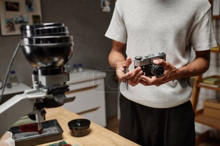 recortado de hombre negro Sujetando intencionadamente una cámara analógica y un bolígrafo mientras está de pie en un laboratorio fotográfico