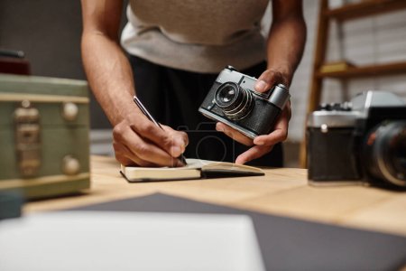 Téléchargez les photos : Recadré afro-américain gars immergé dans l'écriture tenant son appareil photo analogique en studio photo - en image libre de droit