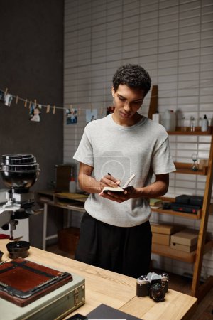 young african american guy immersed in writing standing near analog camera in photo studio