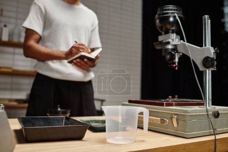 film tray and other photography development equipment near black man with notebook in a darkroom
