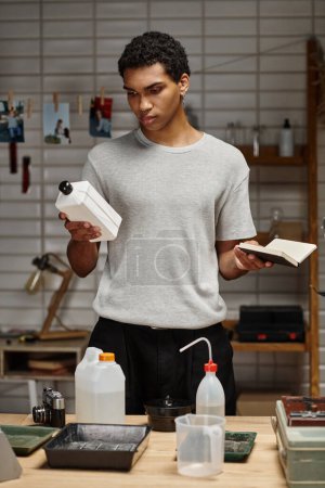 young african american photographer holding chemical solution with notebook, film development