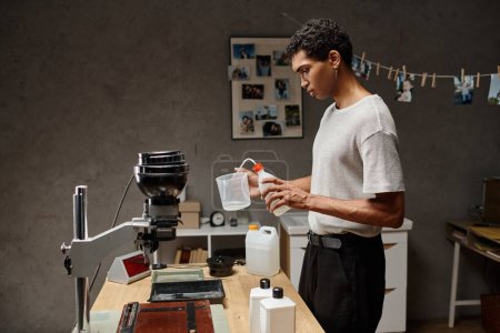 jeune homme afro-américain versant une solution chimique dans une tasse à mesurer, développement de film analogique