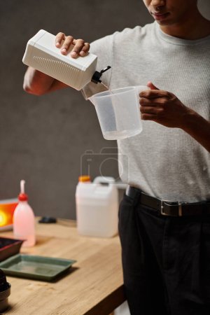 Foto de Hombre afroamericano cultivado verter solución química en taza de medición, desarrollo de películas - Imagen libre de derechos