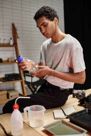 apuesto fotógrafo afroamericano sosteniendo botella con solución química, desarrollo de películas