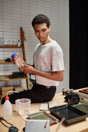apuesto fotógrafo afroamericano sosteniendo botella con solución química, desarrollo de películas