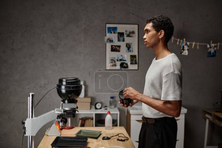apuesto joven afroamericano fotógrafo asegurando una tapa de lata de película en un cuarto oscuro