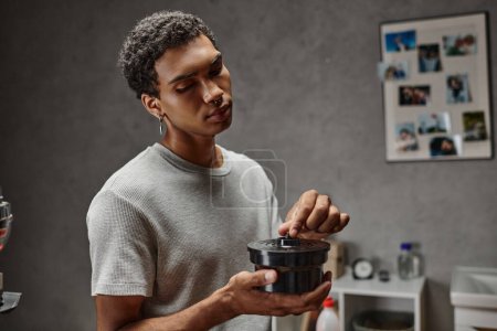joven afroamericano hombre asegurando una tapa de lata de película en cuarto oscuro, fotografía tradicional