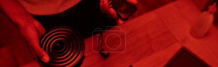Photo for Cropped photographer in red-lit darkroom, black man with timer, banner of film development - Royalty Free Image