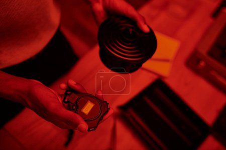 photographer in red-lit darkroom, top view of black man handles film development with darkroom timer