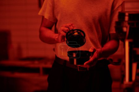 abgeschnittene Aufnahme eines Fotografen, der Filmkanister hält und Fotos in der Dunkelkammer mit Rotlicht entwickelt