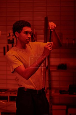 Photographe examine bande de film développé, baigné dans la lumière de la chambre noire rouge, contemplant son travail