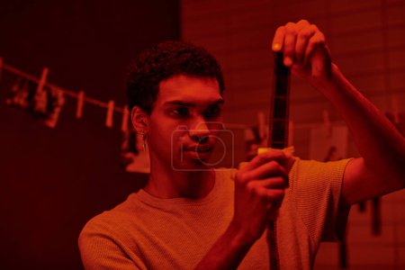 Afrikanisch-amerikanischer Fotograf untersucht entwickelten Filmstreifen, in Dunkelkammer mit Rotlicht gebadet