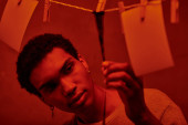young african american man looking at freshly developed film strip  in a red-lit darkroom, nostalgia hoodie #692601284