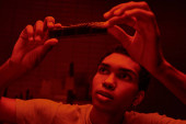 focused african american photographer looking at developed film strip  in a red-lit darkroom hoodie #692601346