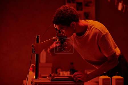 Un photographe méticuleux inspectant la photo négative sous la lumière rouge d'une chambre noire