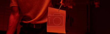 Foto de Pancarta recortada de fotógrafo sosteniendo pinzas con papel fotográfico en un cuarto oscuro con luz roja - Imagen libre de derechos