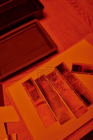 Developed film strips on a table next to darkroom photography equipment, in red safety light