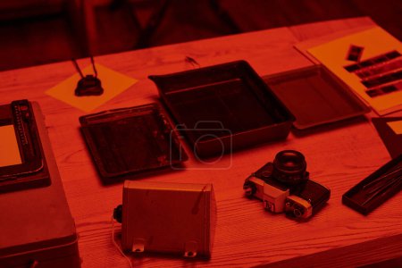 A table with analog camera and tools for film development in darkroom with red light, nostalgia