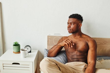 Photo for Young shirtless muscular african american man sitting near bedside table with cup of morning coffee - Royalty Free Image