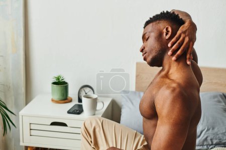 Photo for Athletic shirtless man african american man stretching neck near coffee on bedside table in bedroom - Royalty Free Image
