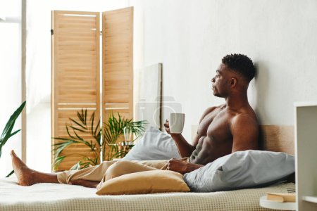 Foto de Hombre afroamericano sin camisa de ensueño con taza de café sentado en la cama y mirando hacia otro lado en la mañana - Imagen libre de derechos