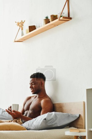 Photo for Joyful african american man with shirtless muscular torso sitting with cup of coffee in bedroom - Royalty Free Image