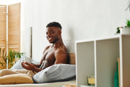 Photo for Happy african american man with muscular body sitting with coffee cup looking at camera in bedroom - Royalty Free Image