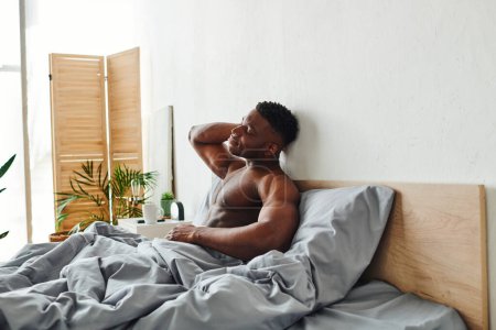 Photo for Pleased african american man with shirtless muscular body and closed eyes sitting on bed in morning - Royalty Free Image