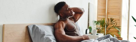 young african american man with closed eyes and muscular torso sitting and stretching on bed, banner