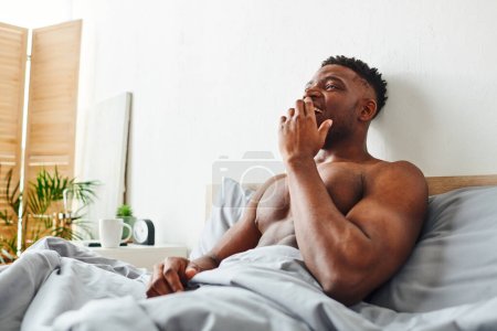 happy shirtless african american man with strong body waking up and yawning on bed in morning