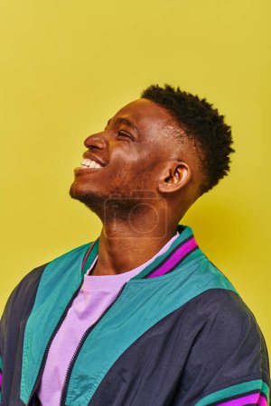 Porträt eines lachenden afrikanisch-amerikanischen Mannes in trendiger Freizeitkleidung, der vor gelbem Hintergrund wegschaut