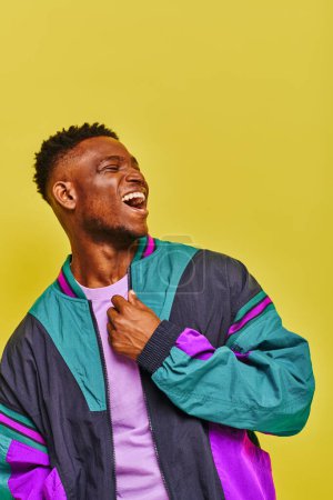 Téléchargez les photos : Émotionnel homme afro-américain en tenue décontractée à la mode rire et détourner les yeux sur jaune - en image libre de droit