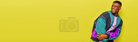 Téléchargez les photos : Joyeux homme afro-américain en tenue décontractée tendance rire et détourner les yeux sur jaune, bannière - en image libre de droit