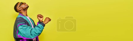 Téléchargez les photos : Énergique homme afro-américain à la mode en veste et lunettes de soleil dansant sur jaune, bannière - en image libre de droit
