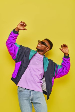 Téléchargez les photos : Heureux homme afro-américain en tenue décontractée élégante et lunettes de soleil dansant sur fond jaune - en image libre de droit