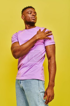 Téléchargez les photos : Jeune homme afro-américain confiant en t-shirt violet vif regardant loin sur fond jaune - en image libre de droit