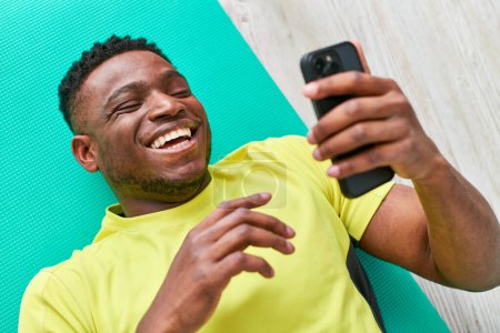 young cheerful african american man in sportswear browsing internet on smartphone, top view