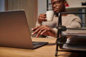 young african american freelancer with coffee cup working at laptop in home office at night puzzle #692608148