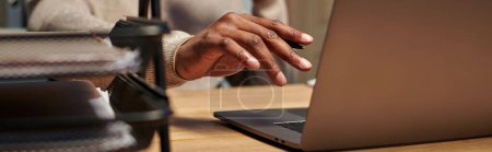 Téléchargez les photos : Vue recadrée de jeune pigiste afro-américain travaillant sur ordinateur portable la nuit à la maison, bannière - en image libre de droit
