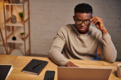serious african american freelancer in eyeglasses thinking near laptop working from home at night Stickers #692608398