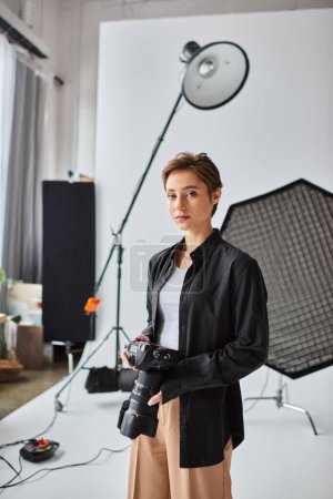 Téléchargez les photos : Attrayant à poil court photographe femme en tenue décontractée regardant la caméra tandis que dans son studio - en image libre de droit