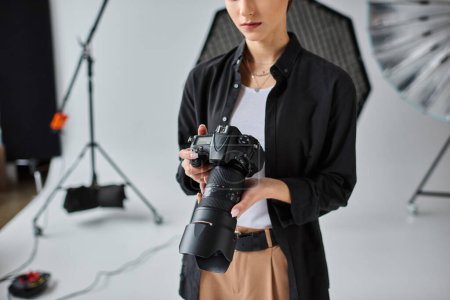 abgeschnittene Ansicht einer jungen Fotografin in lässigem Outfit, die im Studio mit verschiedenen Geräten arbeitet